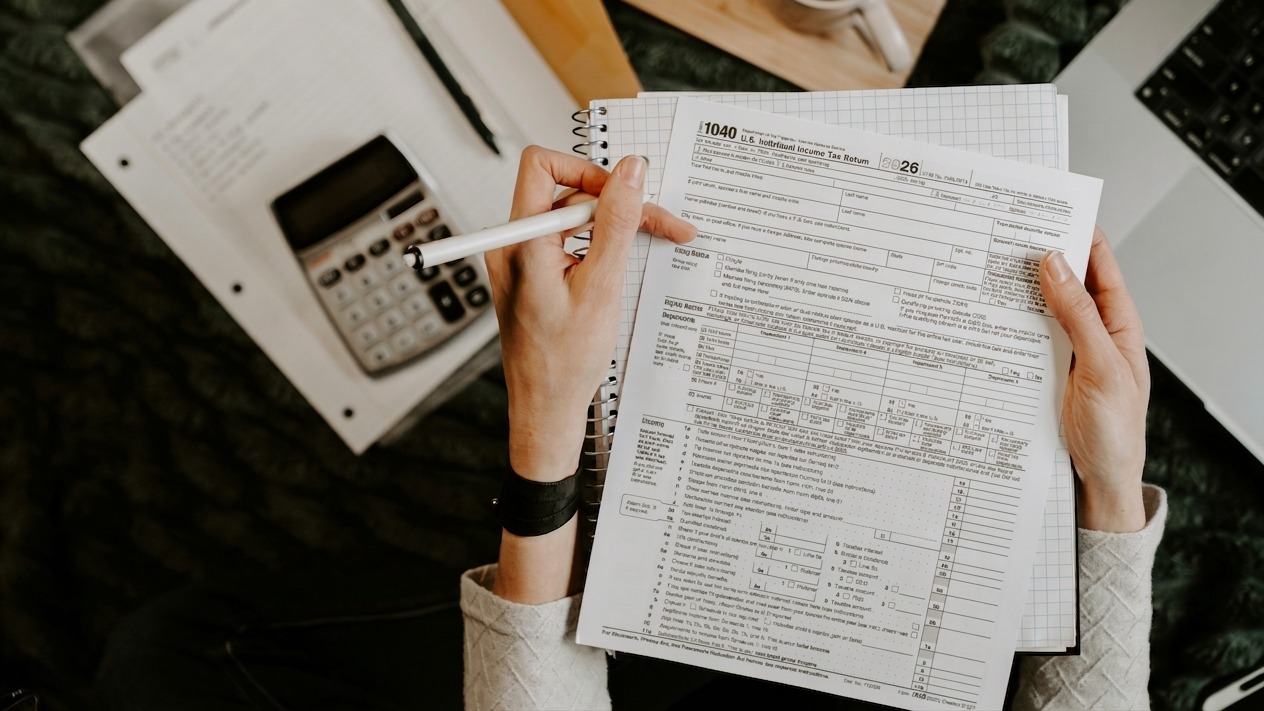 Person reviewing documents with calculator and laptop.