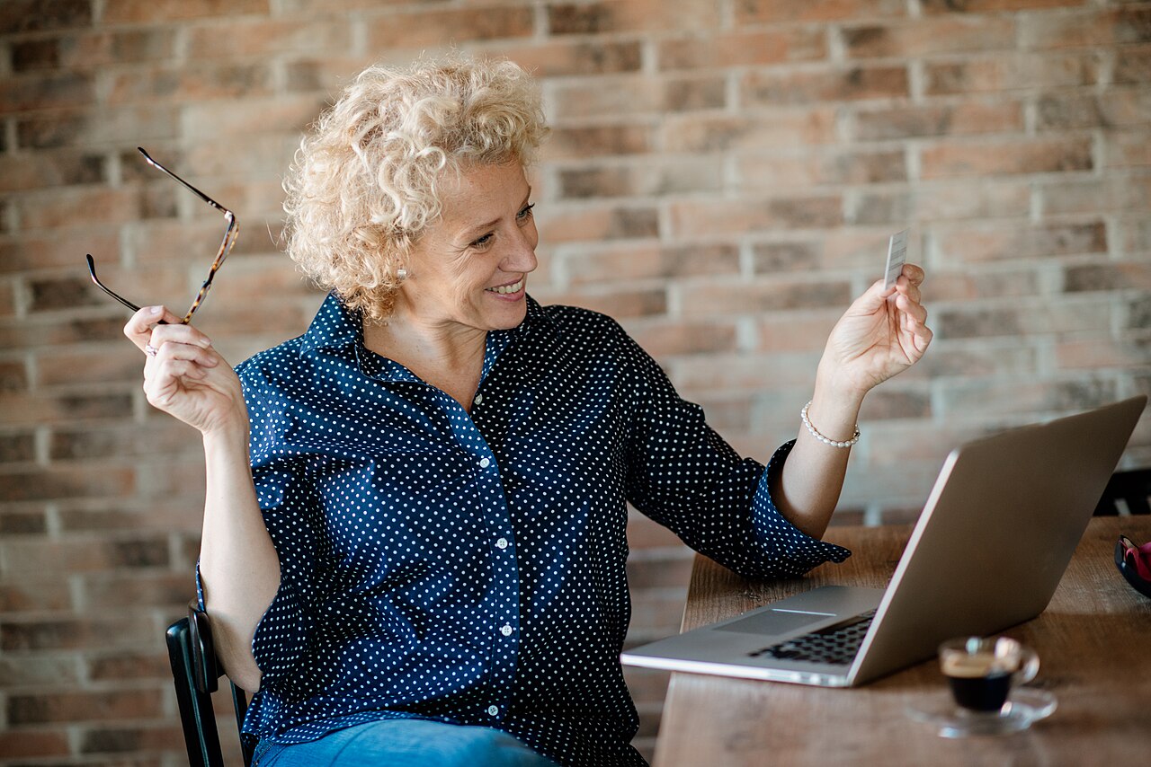 A woman holding a bank card while sitting at a laptop