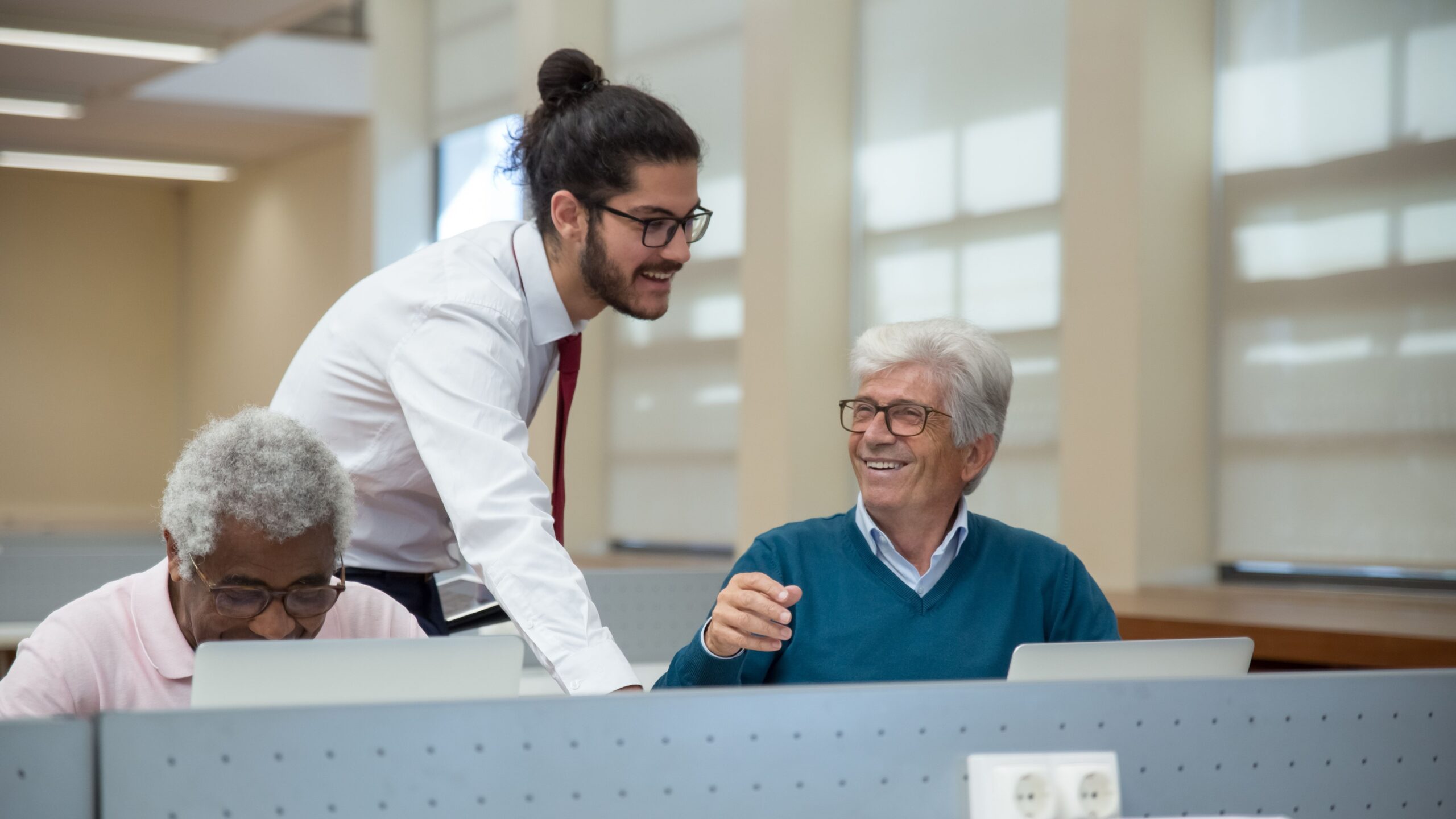 A classroom scene in Portugal where seniors learn computer skills from a young instructor. Engaged and smiling.