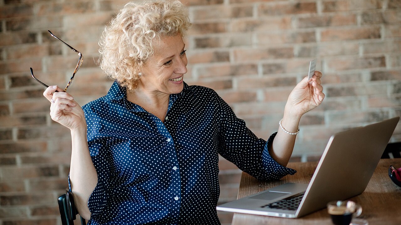 A woman holding a bank card while sitting at a laptop