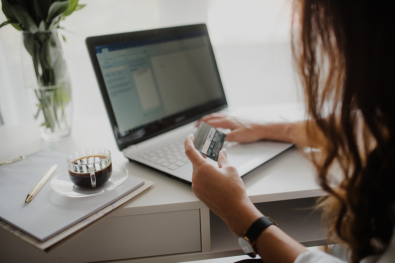 A woman checking her credit card while using a laptop