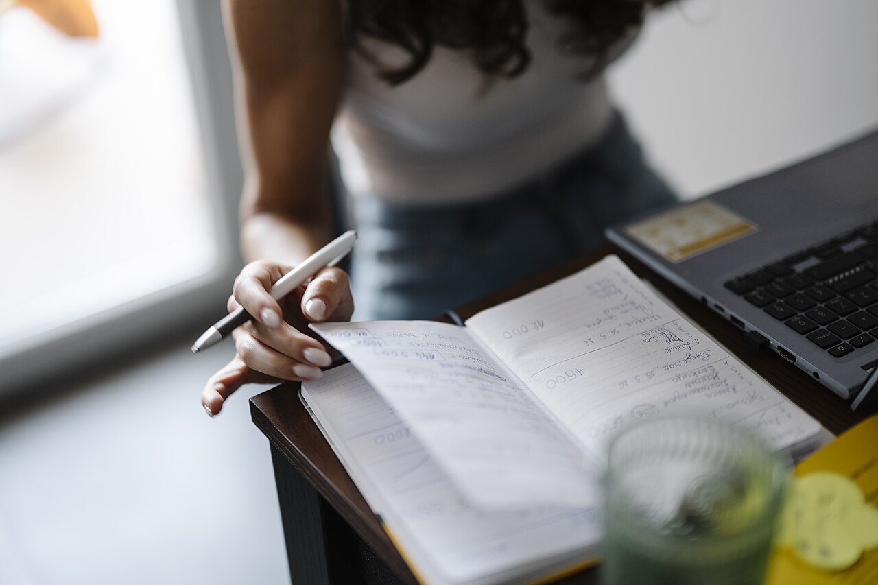 A person writes a note in a notebook at a desk
