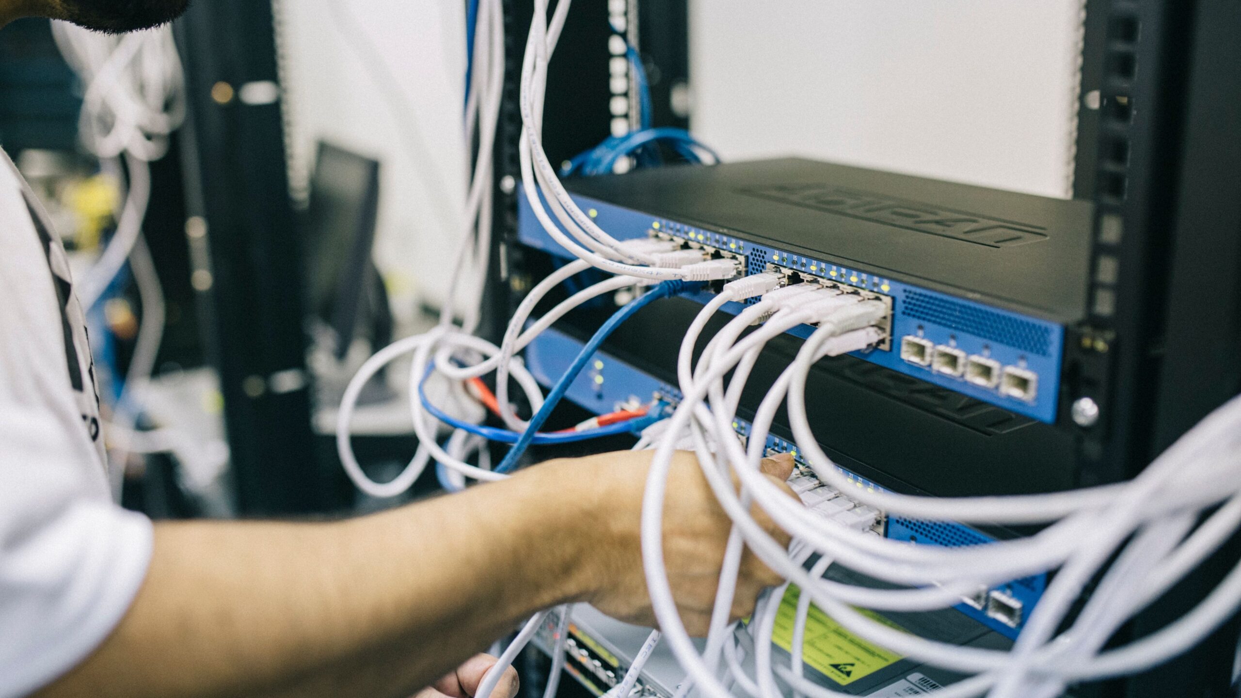 An IT professional configuring network cables in a server rack, focusing on Ethernet connections.