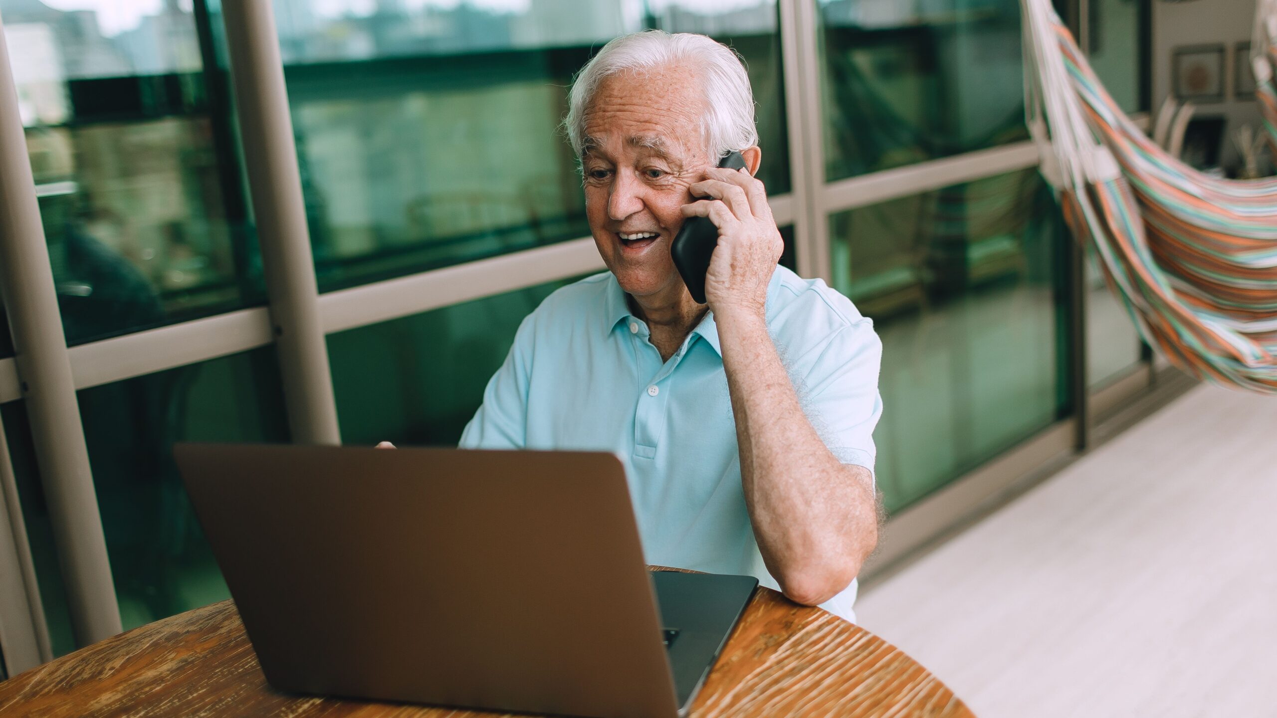 Elderly man in casual setting using a laptop and smartphone indoors, reflecting modern communication.