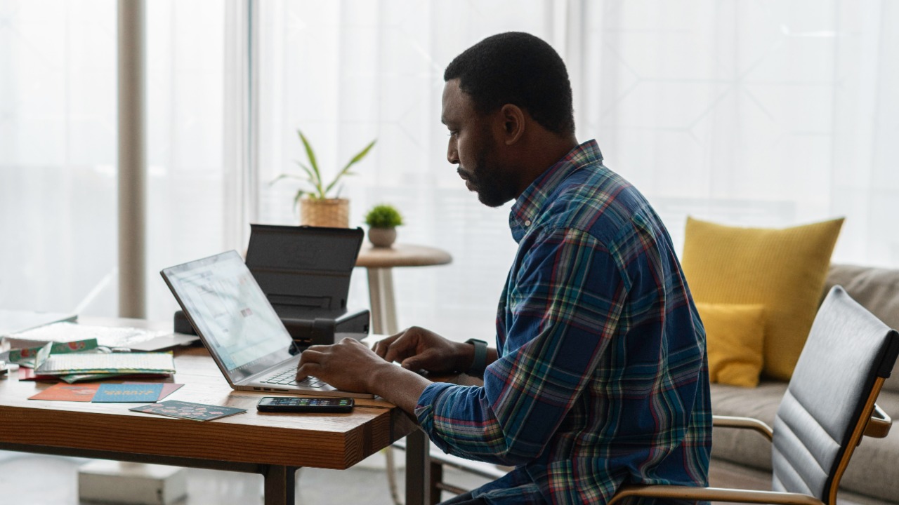 man in blue and white plaid dress shirt sitting on chair using laptop computer